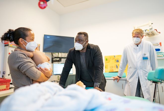 Baby Jack auf dem Arm seiner Mutter, die sich im Krankenhauszimmer mit Gerald Asamoah und Dr. Scheid unterhält