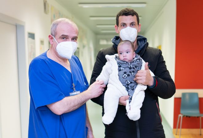 Säugling Amine auf dem Arm seines Vaters und Dr. Gleb Tarusinov stehen auf dem Stationsflur im Herzzentrum Duisburg